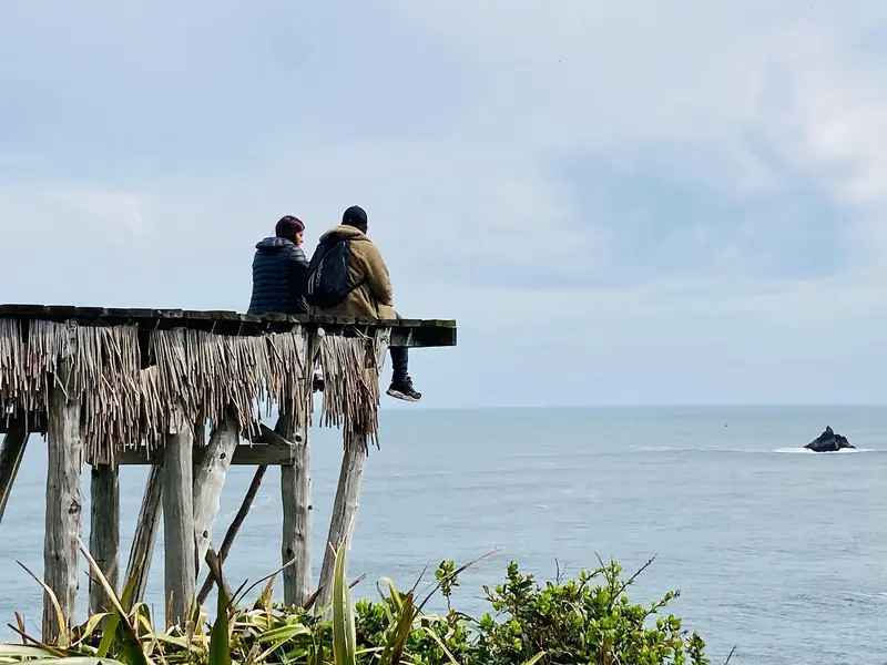 Dos viajeros sentados al borde de un muelle rústico sobre el mar en Chepu